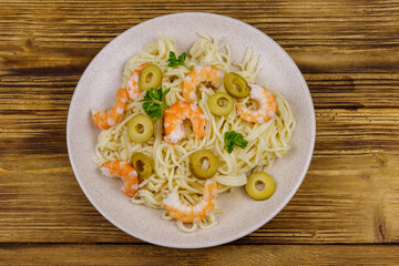 Spaghetti pasta with prawns, green olives and parsley on wooden table. Top view