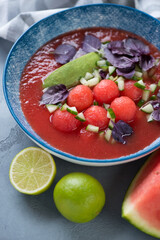 Close-up of tomato and watermelon gazpacho topped with watermelon balls, avocado, chopped cucumber and red basil leaves, vertical shot