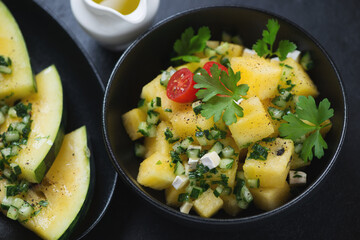 Salad with yellow watermelon cubes, herbed cucumber and fresh parsley in a black bowl, selective focus, closeup