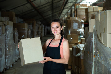 Happy female seller holding box in warehouse. High quality photo