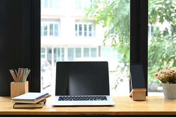 Modern workspace with blank screen laptop,  pencils, smart phone, notebooks and vase on wooden table.