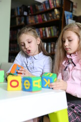 Fototapeta premium Two funny girls playing with alphabet blocks in the library