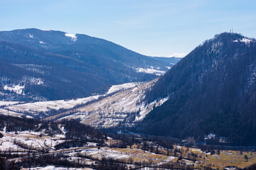 mountainous countryside in early spring. dry grass and leafless trees on the hillside. snow in the distant valley and ridge