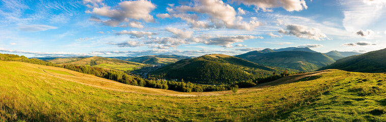 Fototapeta na wymiar mountainous countryside landscape. panorama of a grassy rural field on the hill. village in the distant valley. clouds on the sky