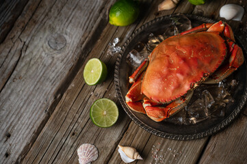 Close-up view of metal black round plate with whole cooked crab and ice cube on wooden background...