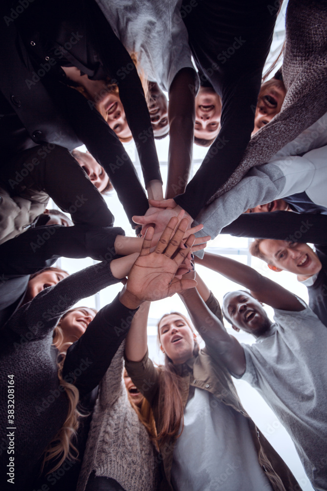 Wall mural bottom view. group of happy young people making a stack of hands