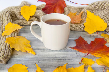 Autumn background with a Cup of tea, berries and yellow leaves on a painted wooden surface.