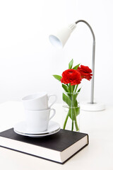 pile of teacups on book, vase and desk lamp