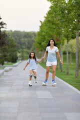 Young mother and her cute little daughter rollerskating in summer park. family concept