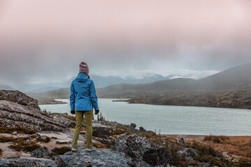 Travel alone in Alaska during cold autumn weather. Woman tourist hiking near lake in the North.