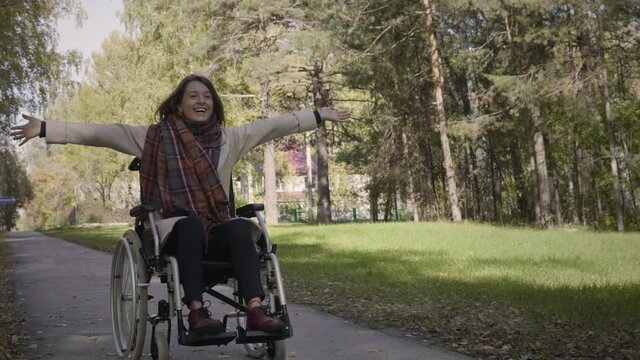 Happy cheerful disabled woman in the wheelchair enjoying the walk in the beautiful autumn forest. Woman is laughing and feels exciting