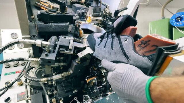Industrial worker is using a mechanism to produce sneakers. Footwear production facility.
