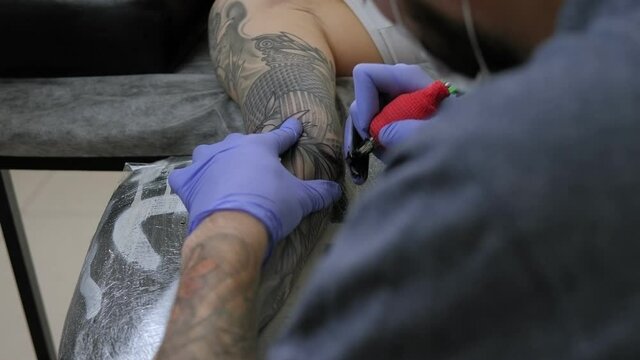 Close-up of a man in blue gloves getting a tattoo on a young woman's arm in a beauty salon.