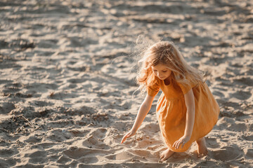 little blonde girl plays on the river in the sand against the sunset sky