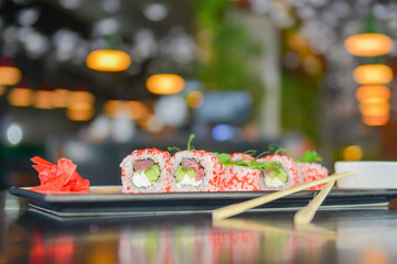 Salmon and caviar sushi rolls served on a traditional plate on a wooden table in a restaurant.