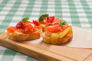 Delicious fruit salmon bruschetta with sauce served on a wooden board over green plaid table cloth.