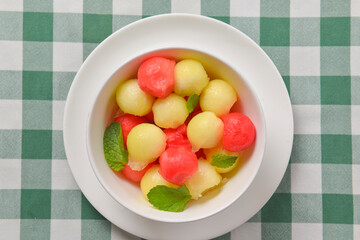 Watermelon granita ice cream. Melon and watermelon sorbet ice cream balls in a white bowl over green plaid table cloth.