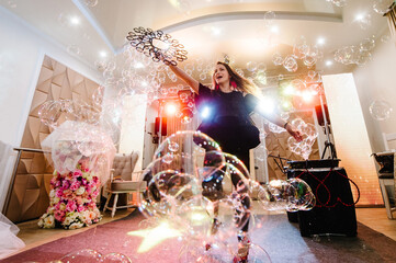 Show soap bubbles. Woman artist blowing many soap bubbles in birthday or wedding party. Happy beautiful girl makes big soap bubbles indoors.