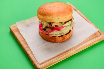 Home made burger on wooden tray over white table cloth and bright green background. Junk food, fast food concept.