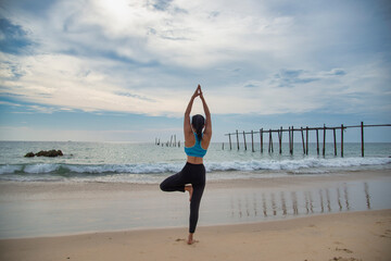 Fototapeta na wymiar Caucasian young woman practicing yoga or fitness at seashore at sunset in the nature