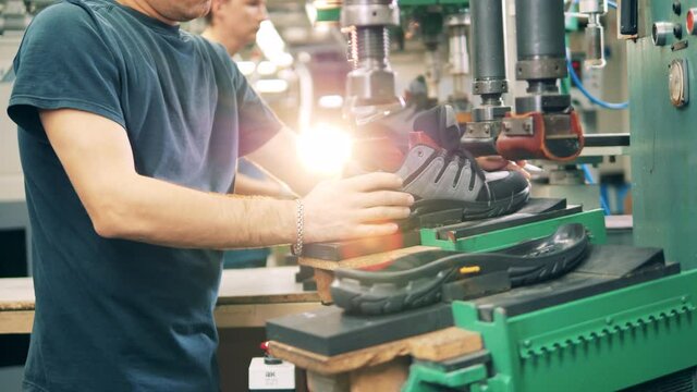 Industrial worker is putting together a boot and its sole