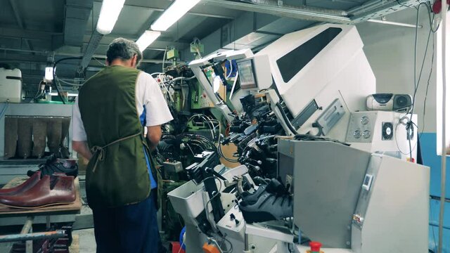 Male workers are using machinery to make shoes. Footwear production facility.