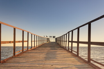 Old wooden pier with railings at sunset. Close-up of a wooden jetty going out to sea against a background of sunset color. Closed exit and seagulls on the railing. 