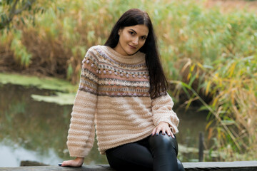 Black-haired woman posing in autumn park in knitted sweater
