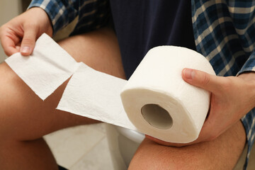 A man sits on the toilet and hold toilet paper