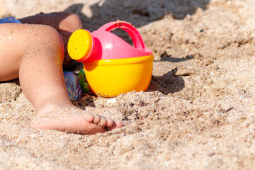 Fototapeta na wymiar child playing with toy watering can on the beach on asummer day