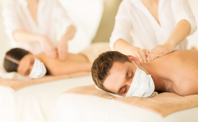 Fototapeta na wymiar wellness, bodycare and health concept - couple wearing face protective medical mask for protection from virus disease having back massage at spa