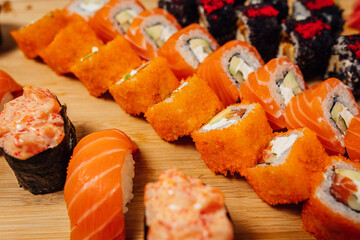 Different type of sushi rolls on wooden board with ginger, wasabi and chop sticks, sushi set on table