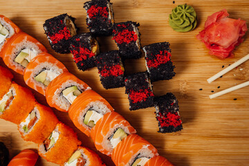 Different type of sushi rolls on wooden board with ginger, wasabi and chop sticks, sushi set on table