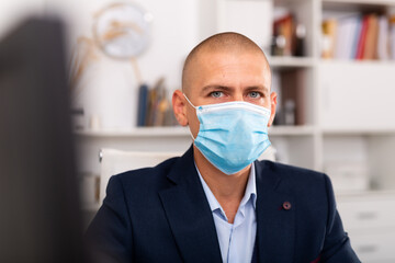 Portrait of young man manager in medical mask standing in modern office