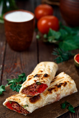 Adana kebab - cooked dish on a wooden background - shish with tomatoes on pita with vegetables and spices. Eastern Arabic or Turkish cuisine, close-up, shallow depth of field