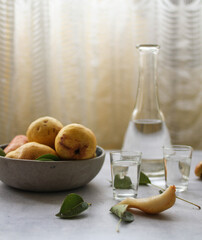 A bottle of Pear Brandy and shot glasses served on a table, with a bowl of fresh pears and pear slices. Brandy Vertical photo.
