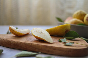 Pear slices cut on the wooden cutting board and bowl of fresh pears on the table. 