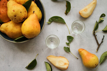 Fresh pears in a bowl, pear slices, and leaves, and a two-shot glasses of pear brandy served on the table. Top view, vertical photo. 