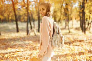 Pretty girl walking at autumn park with fallen leaves in hands, colorful foliage and sunlights on background. Autumn walk concept