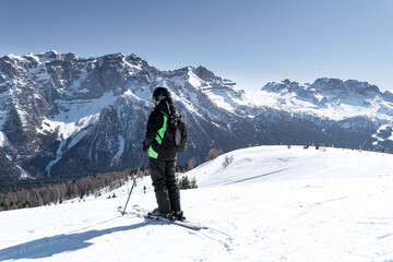 Naklejka na ściany i meble A man stands on the side of a mountain against the backdrop of the snow-capped Dolomites. Concept for sports, landscape, people.