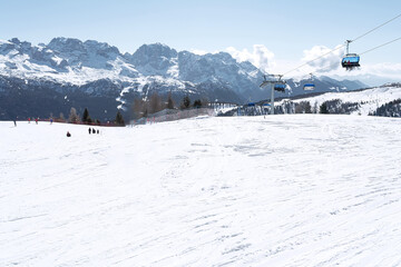 View of the ski slope in the Dolomites with people and the cable car with blue chair lifts. Concept for sports, landscape, people.