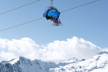 A view of the snow-capped mountains and the cable car with blue chair cabins in which children ride. Concept for sports, landscape, technology.