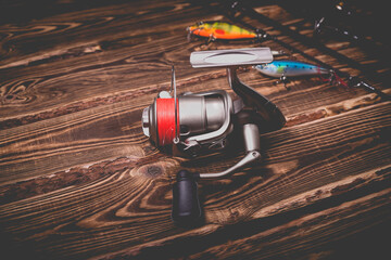Studio photo of fishing tackle on a wooden background. A rod, a reel with a line and three wobblers.