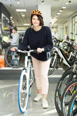 .Smiling young woman in helmet standing with bicycle in the bicycle store..