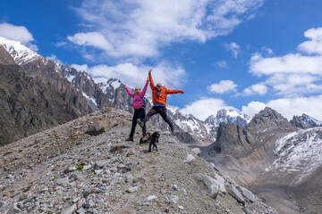 Not young spouses and their dog climbed to a height of 3300 meters above sea level. They are very happy that they were able to go so far. They jump, laugh against the background of snowy mountains.