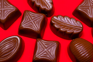 Chocolates made from milk chocolate on a red background macro-shooting close-up. Sweet food, sugar and cocoa. Pastry shop, candy.