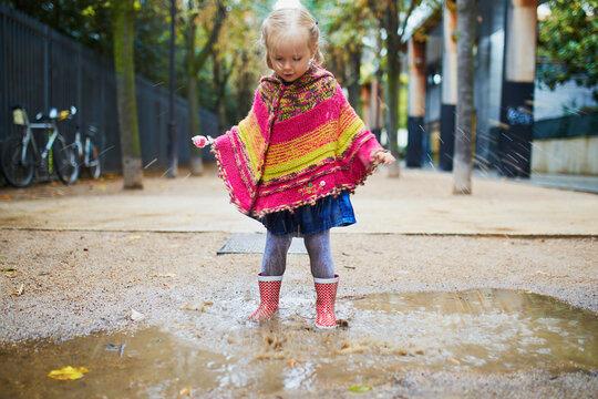 Child Wearing Red Rain Boots And Jumping In Puddle On A Fall Day