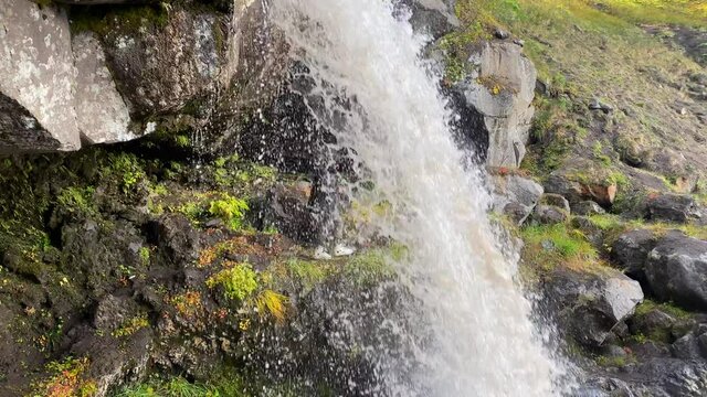 Photographer stands under a beautiful picturesque waterfall and takes pictures of nature. Amazing autumn landscape. Travel to the Kamchatka Peninsula.