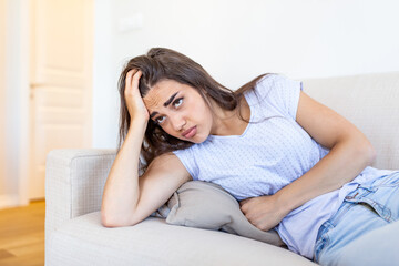 Woman lying on sofa looking sick in the living room. Beautiful young woman lying on bed and holding hands on her stomach. Woman having painful stomachache on bed, Menstrual period