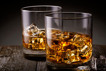 Two glasses of whiskey with ice cubes on wooden table.